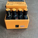 Oranžový efekt pedál s černým ovládacím panelem a čtyřmi černými otočnými knoflíky. Na horní části je nápis TURBO Distortion DS-2 a označení vstupů I…
