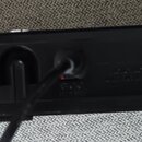 Zadní strana černého elektronického zařízení s bílými krajními částmi. Na levé straně je vyražen nápis AX5 MODSUNG SIGNAL PROCESSOR. V prostřední čás…