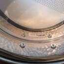 Detailní pohled na kovový nástroj s kovaným, nepravidelným povrchem. Na obruči je vidět bílá náleplka s nápisy „Hand Hammered“, „Made in India“ a čár…