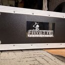 Stříbrný hliníkový přepravní kufr s černým předním panelem. Uprostřed panelu je nálepka s logem kostry a nápisem FRYETTE AMPLIFICATION. Rohy kufru js…