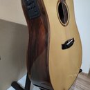 Akustická kytara s cutawayem, světlou deskou a tmavě hnědými boky z dřeva. Na boku je umístěn černý ovládací panel s knoflíky a přepínačem. Nástroj j…