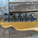 Detail hlavy kytary z jasného dřeva s šesti chromovanými ladicími mechanismy. Na každém mechanismu je vidět nápis JAPAN a FENDER. Povrch dřeva i kovo…