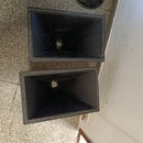 Dvě černé plastové akustické trouby s hranatým tvarem. Povrch je matný a v horní části jsou vidět drobné nečistoty a prach. Na fotce nejsou žádné vid…