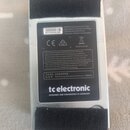 Fotografie zachycuje zadní stranu stříbrného efektpedálu. Na černé štítku je uveden nápis tc electronic DESIGNED AND ENGINEERED IN DENMARK, kód S2101…