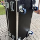 Černý transportní flightcase s hliníkovými hranami a rohy. Bedna je vybavena čtyřmi modrými kolečky, dvěma madly a kovovými zapínacími zámky. Povrch…