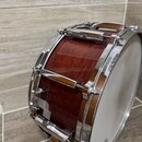 Dřevěný buben s hnědým povrchem a chromovaným kováním. Na bílém koženu je vidět část loga s nápisem "Pearl". Horní chromovaný obruč vykazuje v pravé…