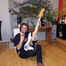 Fotografie zachycuje muže s elektrickou basovou kytarou. Nástroj má bílé tělo, černý pickguard a světle hnědý javorový krk. Na hlavě nástroje je vidi…