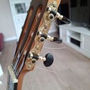 Detail hlavy klasické kytary z hnědého dřeva. Na hlavě jsou zlaté ozdobné kovové płytky s vyrytým ornamentem a tři ladicí mechanismy s černými knoflí…