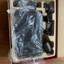 Fotografie znázorňuje otevřenou kartonovou krabici s vložkou, ve které se nachází elektronické zařízení zabalené v průhledném plastovém sáčku. Vedle…
