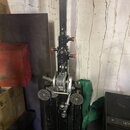 Fotografie zachycuje detail kovového mechanismu s černým profilem a stříbrnou cívkou s navinutým drátem. Na mechanismu jsou vidět červené ovládací kn…