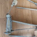 Kovový mechanismus pedálu s nápisem Amati v kurzivním písmu. Povrch vykazuje známky opotřebení, oxidaci a drobné škrábance. Vedle mechanismu leží něk…
