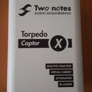 Bílý obdélníkový box s nápisy v černé barvě. V horní části je logo a text Two notes AUDIO ENGINEERING, uprostřed nápis Torpedo Captor X. Ve spodní čá…