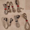 Sada šesti šedých audio kabelů různých délek, z nichž některé jsou svázány červenými nebo černými stahovacími pásky. Kabely mají konektory typu XLR a…