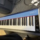 Modrý digitální klavír s bílými a černými klávesami. Na horní části je nápis VIVO S1 a v pravém dolním rohu logo T2L Modeling. Na pravé straně se nac…