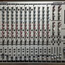 Stříbrný míchací pult s nápisy BEHRINGER® ULTRA-LOW NOISE DESIGN a EURORACK MX 2642A 26 INPUT 4-BUS MIXING CONSOLE. Zařízení obsahuje řady šedých, mo…