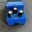 Modrý efekt pedál s nápisy Compression Sustainer CS-2 a značkou BOSS. Na horní straně jsou označení INPUT a OUTPUT u vstupních konektorů. Přístroj má…
