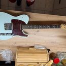 Světle modrá elektrická kytara typu Telecaster s červeně hnědým vzorovaným pickguardem a hnedým hmatníkem. Na hlavě kytary je vidět nápis Fender TELE…
