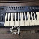 Černý kompaktní MIDI kontrolér s klávesnicí, umístěný na dřevěném stole. Na levé straně je bílý nápis ALESIS QX25 a ovládací prvky v podobě tlačítek,…