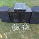 Sada zvukové techniky složená z mixážního pultu, dvou černých reproduktorů a dvou černých krytů z látky. Na přední straně obou reproduktorů je umístě…