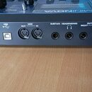 Detail zadní strany černého elektronického nástroje s řadou konektorů. Jsou zde nápisy POWER IN 9V DC 300mA, ext DC OFF, USB, MIDI OUT a IN, SUSTAIN,…