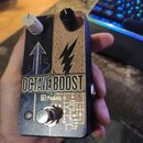 Kytarový efekt pedál v modrém kovovém rámu s grafickým potiskem. Na přední straně je nápis OCTAVE BOOST a logo M pedals, doplněné symboly šipky a ble…