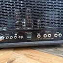 Detail zadní strany černého kytarového zesilovače s mřížkou, za kterou jsou vidět elektronky. Na ovládacím panelu jsou nápisy SEND, FX LOOP LEVEL, FX…
