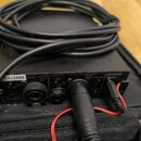 Černý elektronický přístroj s několika konektory a ovládacími prvky. Na předním panelu jsou nápisy LEVEL, PHANTOM, MIC IN 1 a MIC IN 2, dále označení…