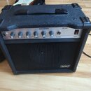 Černý kytarový kombo zesilovač s texturovaným povrchem a stříbrným ovládacím panelem. Na panelu jsou nápisy INPUT, VOLUME, DRIVE, REVERB, TREBLE, BAS…