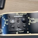 Detail ovládacího panelu s černým plastovým krytem na bílém povrchu nástroje. Na panelu je nápis FISHMAN®, logo Fender a popisky batt, tuner, volume,…