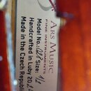 Detailní záběr na vnitřní štítek hudebního nástroje. Na bílém pozadí je uveden nápis Ars Music FINE INSTRUMENTS, Model No.: 028 Size: 1/2, Handcrafte…