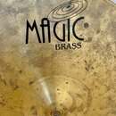 Detailní pohled na mosazný činel zlaté barvy. Na povrchu je černý nápis MAGIC BRASS s logem ve tvaru koncentrických kruhů a symbolem ®. Povrch činelu…