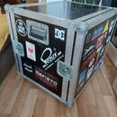 Černý transportní flightcase s hliníkovými hranami a rohovými zpevněními. Povrch je polepený různými nálepkami, mezi nimiž jsou viditelné nápisy SUIC…
