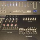 Detailní pohled na černý mixovací pult s nápisem AUDIENT ASP4816 HIGH HERITAGE EDITION. Zařízení obsahuje řadu posuvníků, otočných potenciometrů a bí…