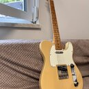 Elektrická kytara typu Telecaster v krémové barvě s bílým pickguardem. Na hlavě hmatníku je viditelné logo Fender. Nástroj je vybaven stříbrným moste…