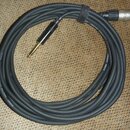 Černý mikrofonní kabel s konektory XLR a 6,3mm jack. Na kabelu je bílý nápis MICROPHONE 2X0,22MM2 CMN220 a COYDOL GERMANY. Kabel je srolovaný do kruh…