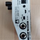 Záběr na zadní stranu bílého elektronického zařízení. Jsou zde vidět konektory POWER, USB, SPEAKER OUT a AMP IN / INST / LINE IN, dále přepínač IN LE…