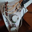 Fotografie zachycuje vnitřek elektroniky elektrokitary s viditelným zapojením vodičů a potenciometrů. Na jednom z potenciometrů je nápis M250k 14 K a…
