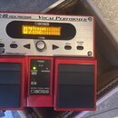 Červený vokální procesor značky BOSS s nápisy VE-20 VOCAL PROCESSOR a Vocal Performer. Zařízení má stříbrný ovládací panel s displejem, na kterém je…