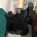 Zadní strana černé elektrické kytary s lesklým povrchem a světlým krkem. Na spojení krku s tělem je vidět kovovádeska se čtyřmi šrouby. V dolní části…