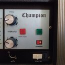 Detail kontrolního panelu zesilovače s nápisem Champion. Panel obsahuje dva stříbrné otočné ovladače s popisky SPEED a VIBRATO, červené a zelené tlač…
