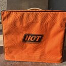 Oranžový textilní kryt na hudební zařízení s černým lemováním okrajů. Uprostřed je umístěno černé logo s nápisem HOT a pod ním text CUSTOM AMPLIFICAT…