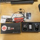 Sada bezdrátového systému pro kytaru značky Xvive. Na fotografii je černá krabice s nápisem Xvive a Wireless Guitar System, otevřený černý obal s dvě…