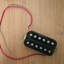 Černý humbucker s dvěma řadami šesti stříbrných pólů. K snímači vede červený elektrický kabel. Snímač je umístěn na dřevěném povrchu a nemá žádné vid…