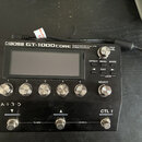 Černý kytarový procesor s nápisy BOSS GT-1000CORE GUITAR EFFECTS PROCESSOR a A.I.R.D. Zařízení má displej, pět stříbrných otočných ovladačů s čísly 1…
