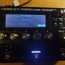 Černý kytarový efektový procesor s nápisem BOSS GT-1000CORE GUITAR EFFECTS PROCESSOR. Zařízení má digitální displej, na kterém je text GT-1000CORE a…