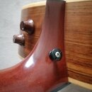 Detailní pohled na spoj hmatníku a krku akustické kytary z tmavého dřeva. Na krku je vidět černý plastový šroub s křížovou hlavou. V pozadí jsou vidě…