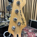 Záběr na hlavu basové kytary z přírodního světlého dřeva. Na povrchu je černý nápis Squier JAZZ BASS by Fender a v horní části menší nápis Standard.…