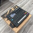 Černý digitální syntetizátor Digitone s malým displejem a řadou ovládacích knoflíků a tlačítek. Na horní části je bílý nápis Digitone a logo Elektron…