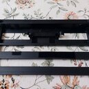 Černý kovový rám s mřížkovou strukturou, který slouží jako základna nebo držák. Na vnitřních hranách jsou nalepené útržky černého suchého zapínání. V…