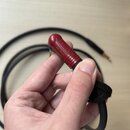Černý kabel s červeným konektorem, který drží ruka. Na červené části konektoru je vyryt nápis NEUTRIK a pod ním slovo SILENT. Kabel je upevněn černým…